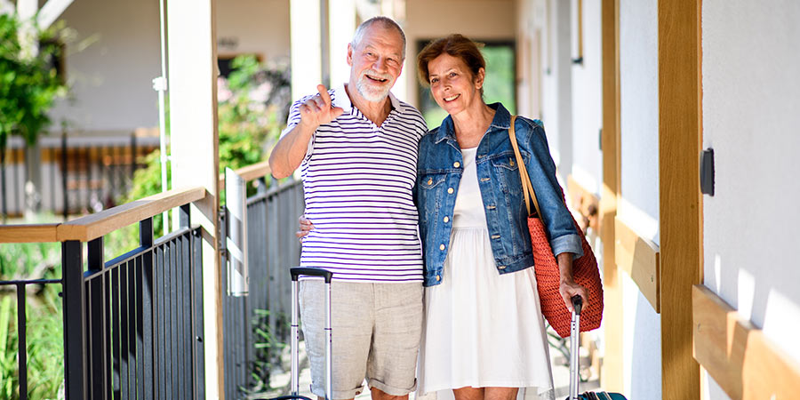 A couple carry their luggage as they stand outside of their holiday accommodation. 