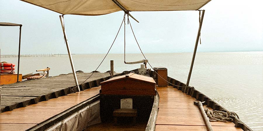 Traditional wooden boat on the lagoon at Albufera Natural Park, viewed onboard from beneath a canopy. 